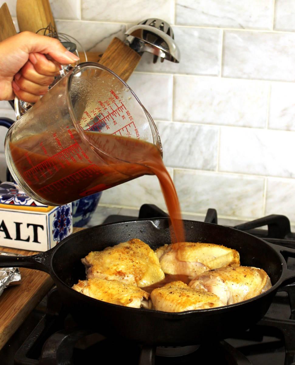 Pepper & Onion Relish Chicken image   hand pouring relish onto chicken in a skillet on a stove.