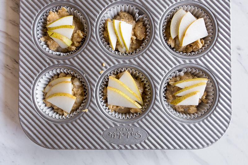 Pear muffins in a tin topped with sliced pears.