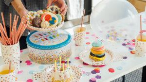 Birthday traditions around the world image   birthday cake and candles on a table with someone setting down a plate of cookies.