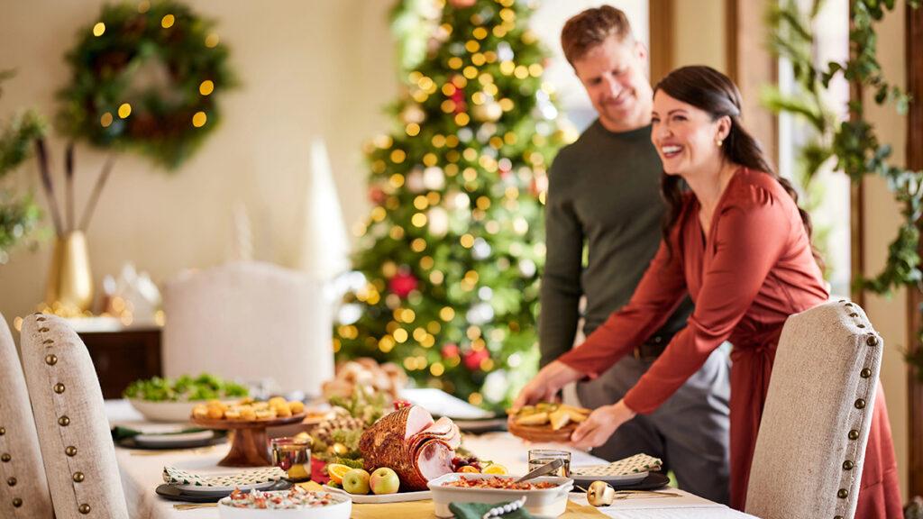 Holiday party table with food and two people laying dishes on top.