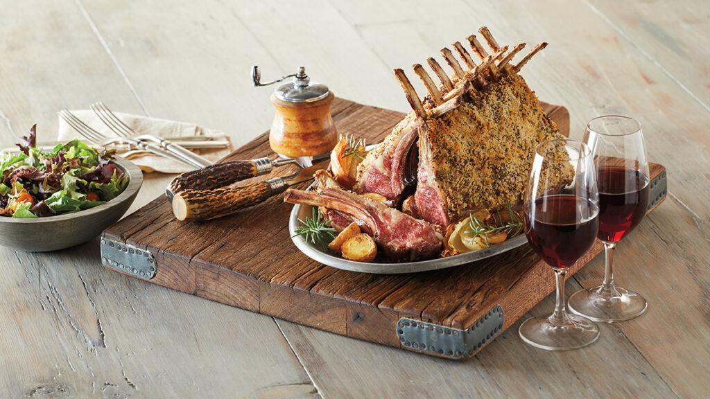 Lamb chops on a plate next to two glasses of wine with a bowl of salad greens.