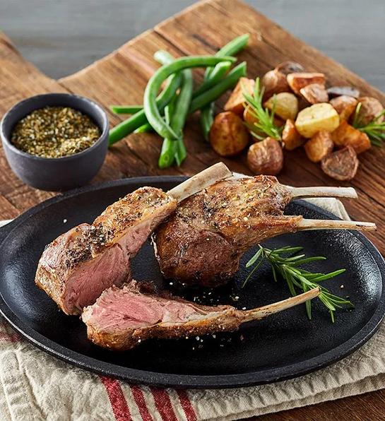 Double cut lamb chops on a black plate with veggies and dipping sauce.