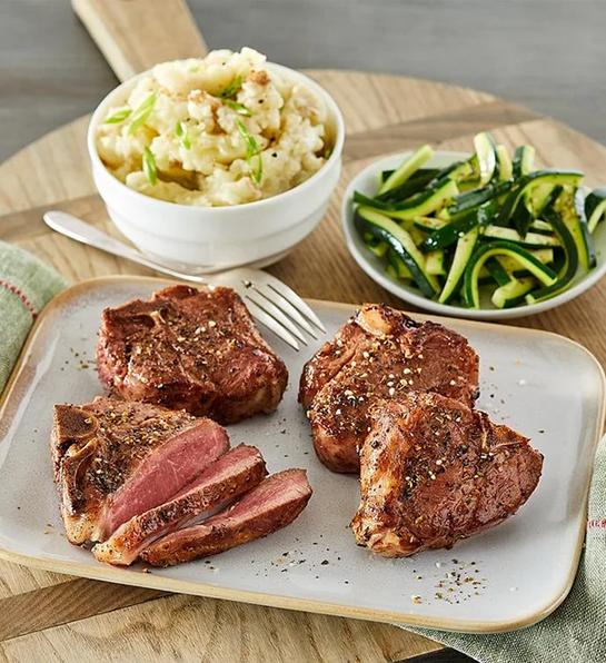 Lamb porterhouse chops on a plate next to veggie side dishes.